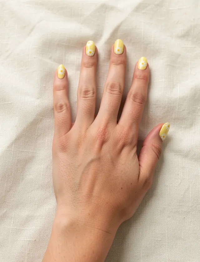 Oval nails in butter yellow polish with small hand-painted white daisies
